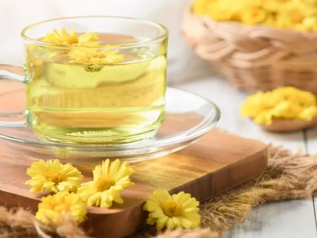 A cup of chrysanthemum tea with petals floating on top, surrounded by dried flowers.